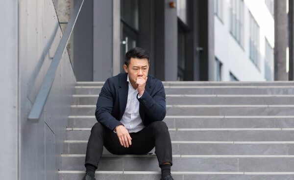 Man sitting overwhelmed with workplace loneliness. Sitting on stairs outside office building.
